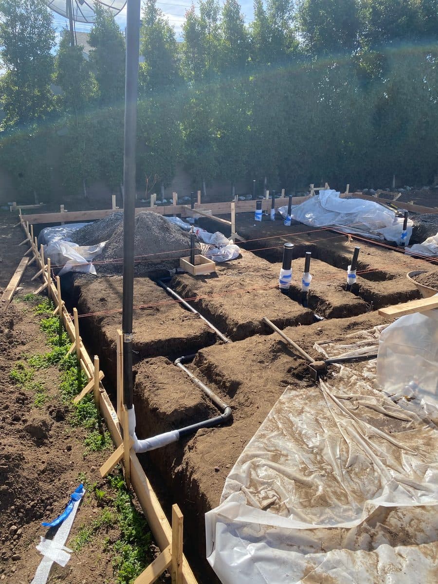 Underground drain lines staked and graded in open trenches at a new build