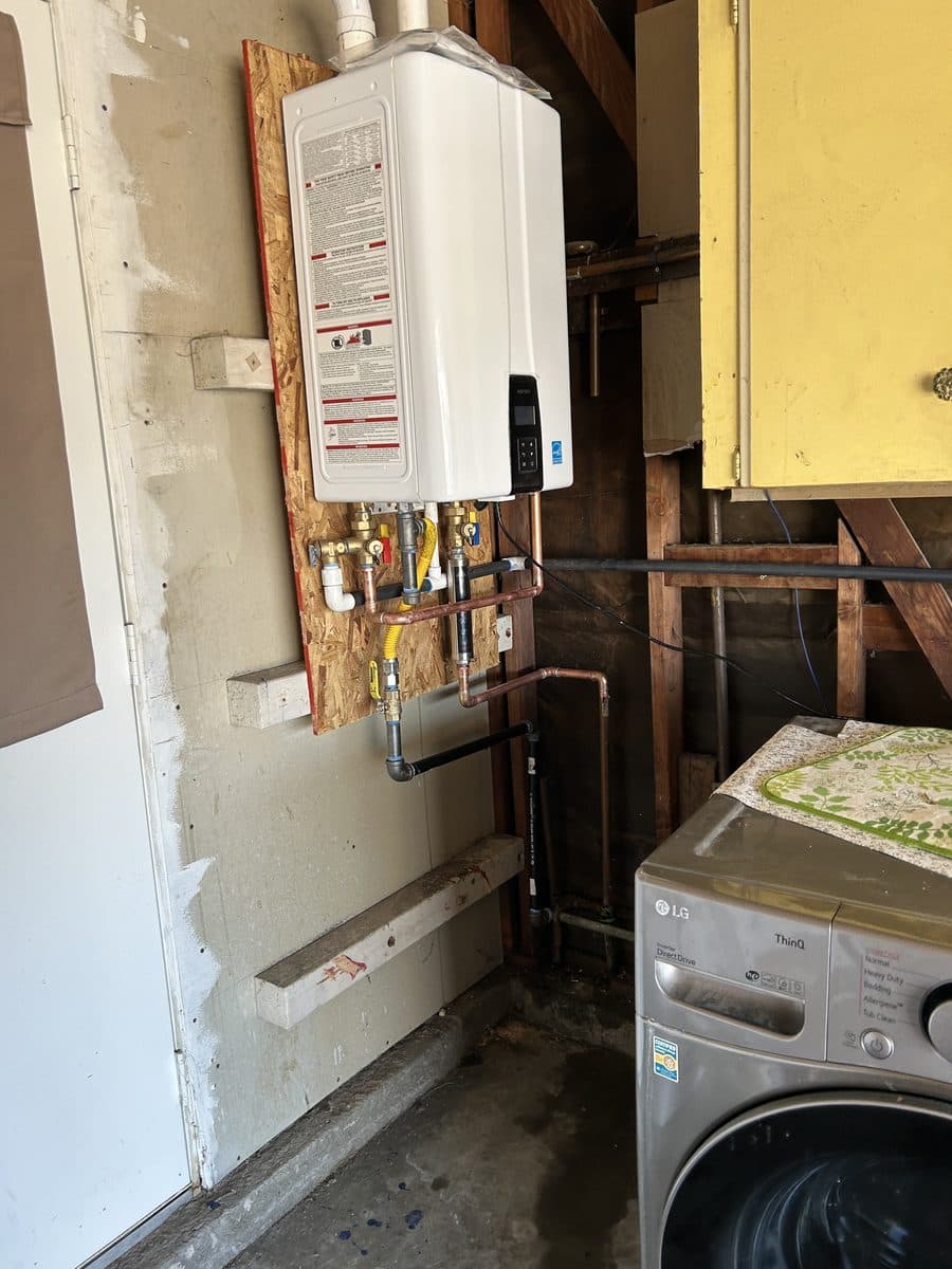 Tankless water heater installed in a laundry area with reworked copper and gas connections